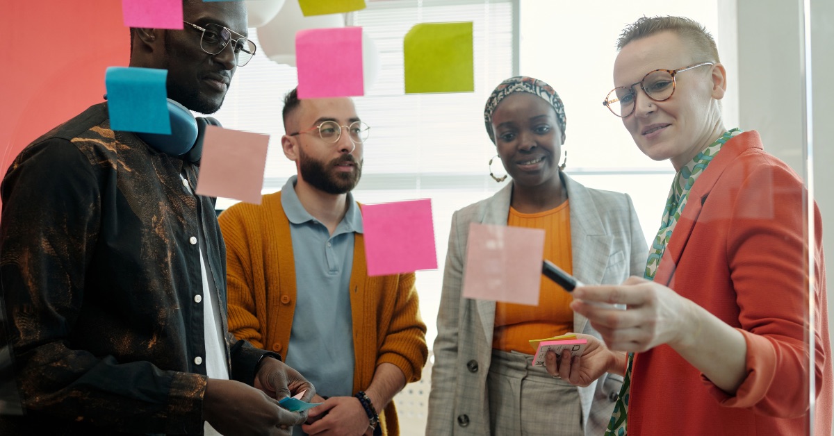 Four colleagues collaborating with colorful sticky notes on a glass wall.
